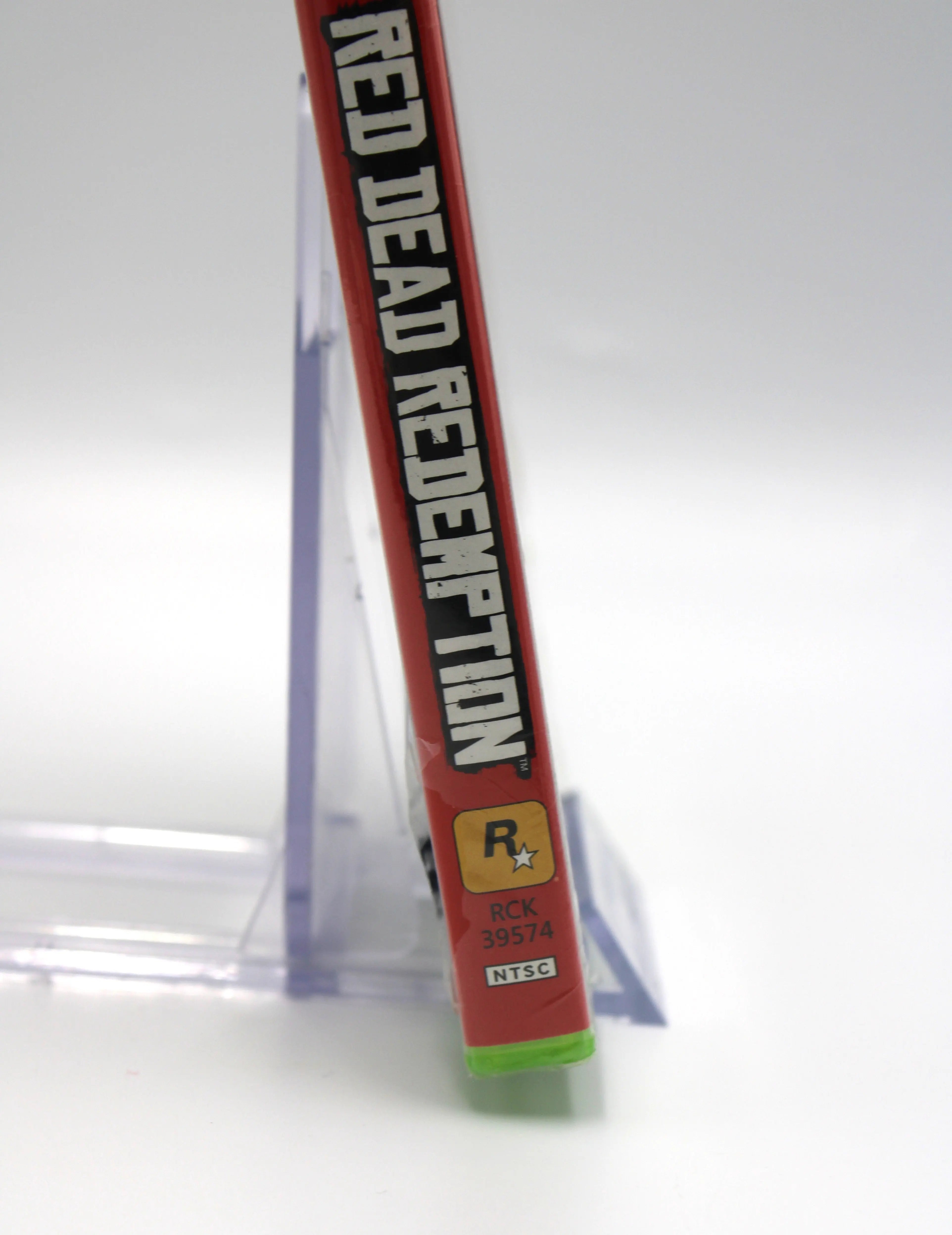 Bottom of spine view of Red Dead Redemption for Microsoft Xbox 360 NTSC-U sealed Platinum Hits game case, showing partial title text , Rockstar logo, Microsoft game code numbers, and sealed packaging with tear at bottom that wraps around.