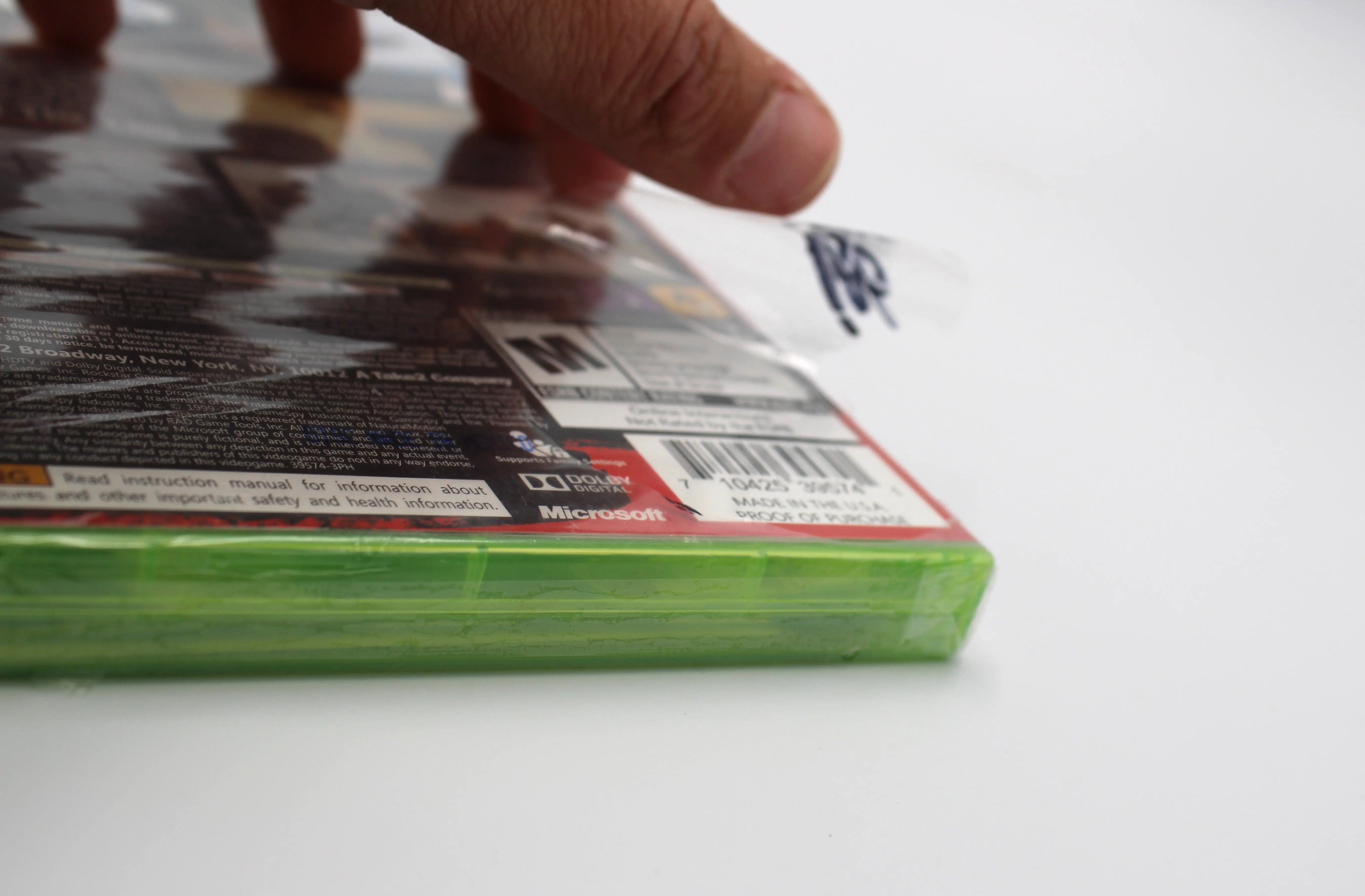 Close-up image of Red Dead Redemption for Microsoft Xbox 360 NTSC-U, showing large tear on factory seal wrap over UPC barcode on back of case.