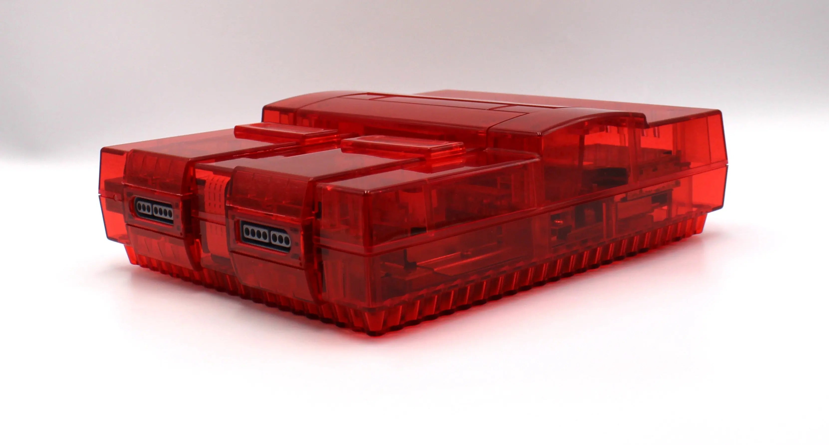 SNES Console Left Angled View: Refurbished Super Nintendo SNES with OEM controller and cables. 1991 NTSC-U console with a new translucent red shell. Image of left side at an angle of the SNES against a clean white background showing refurbished condition.