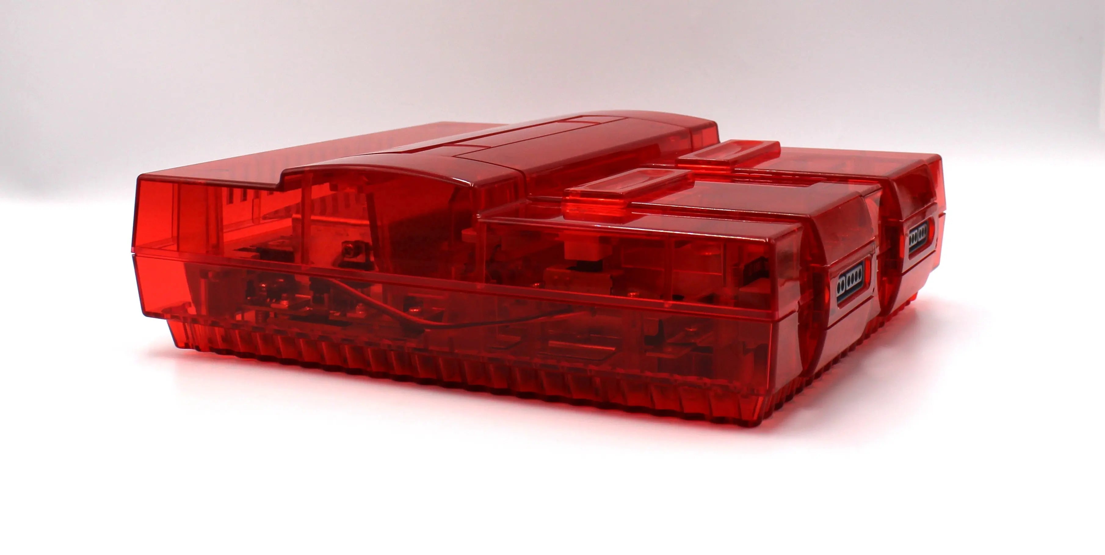 SNES Console Right Angled View: Refurbished Super Nintendo SNES with OEM controller and cables. 1991 NTSC-U console with a new translucent red shell. Image of right side at an angle of the SNES against a clean white background showing refurbished condition.