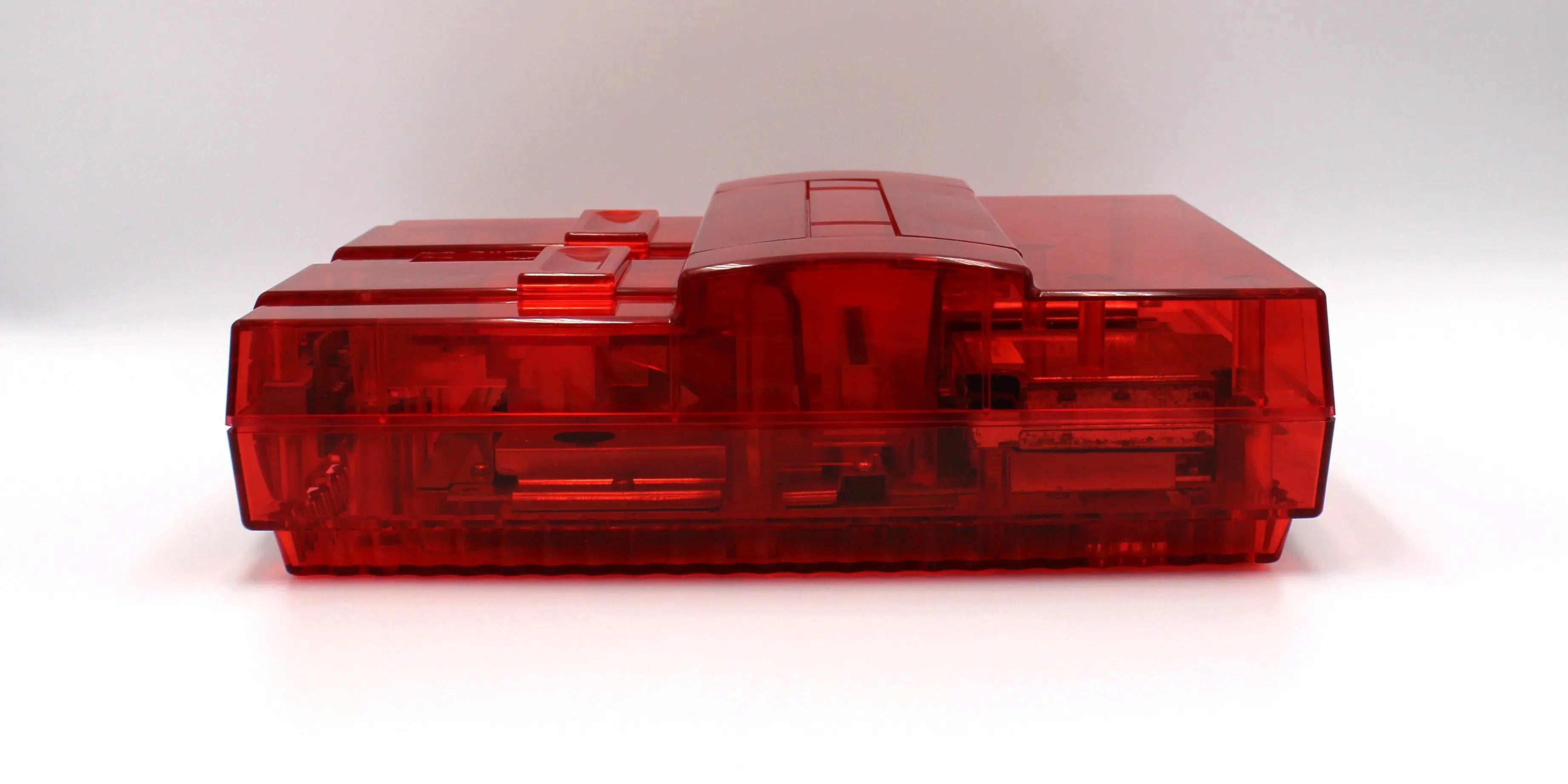 SNES Console Left Side View: Refurbished Super Nintendo SNES with OEM controller and cables. 1991 NTSC-U console with a new translucent red shell. Image of left side of the SNES against a clean white background showing refurbished condition.