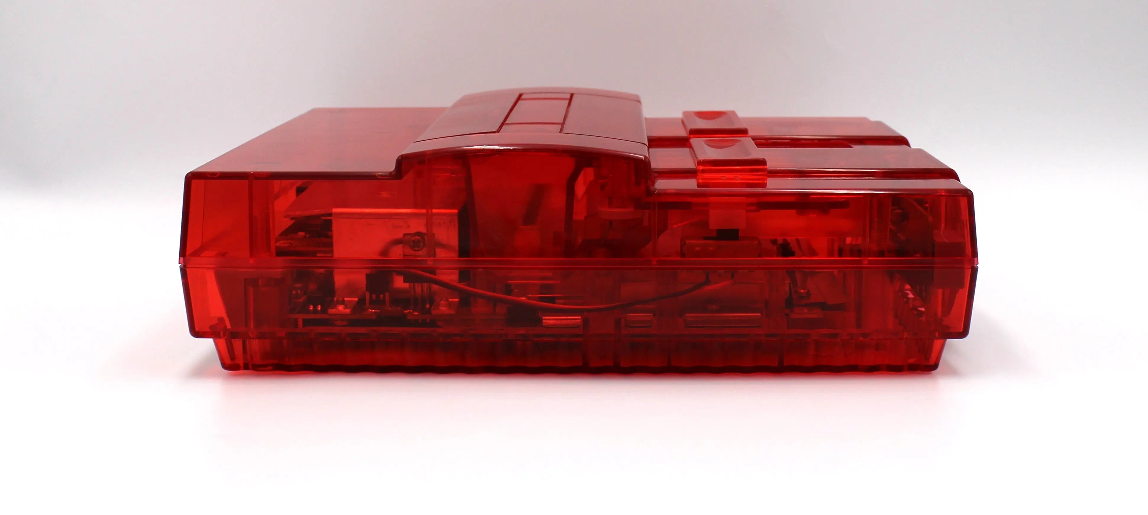 SNES Console Right Side View: Refurbished Super Nintendo SNES with OEM controller and cables. 1991 NTSC-U console with a new translucent red shell. Image of right side of the SNES against a clean white background showing refurbished condition.