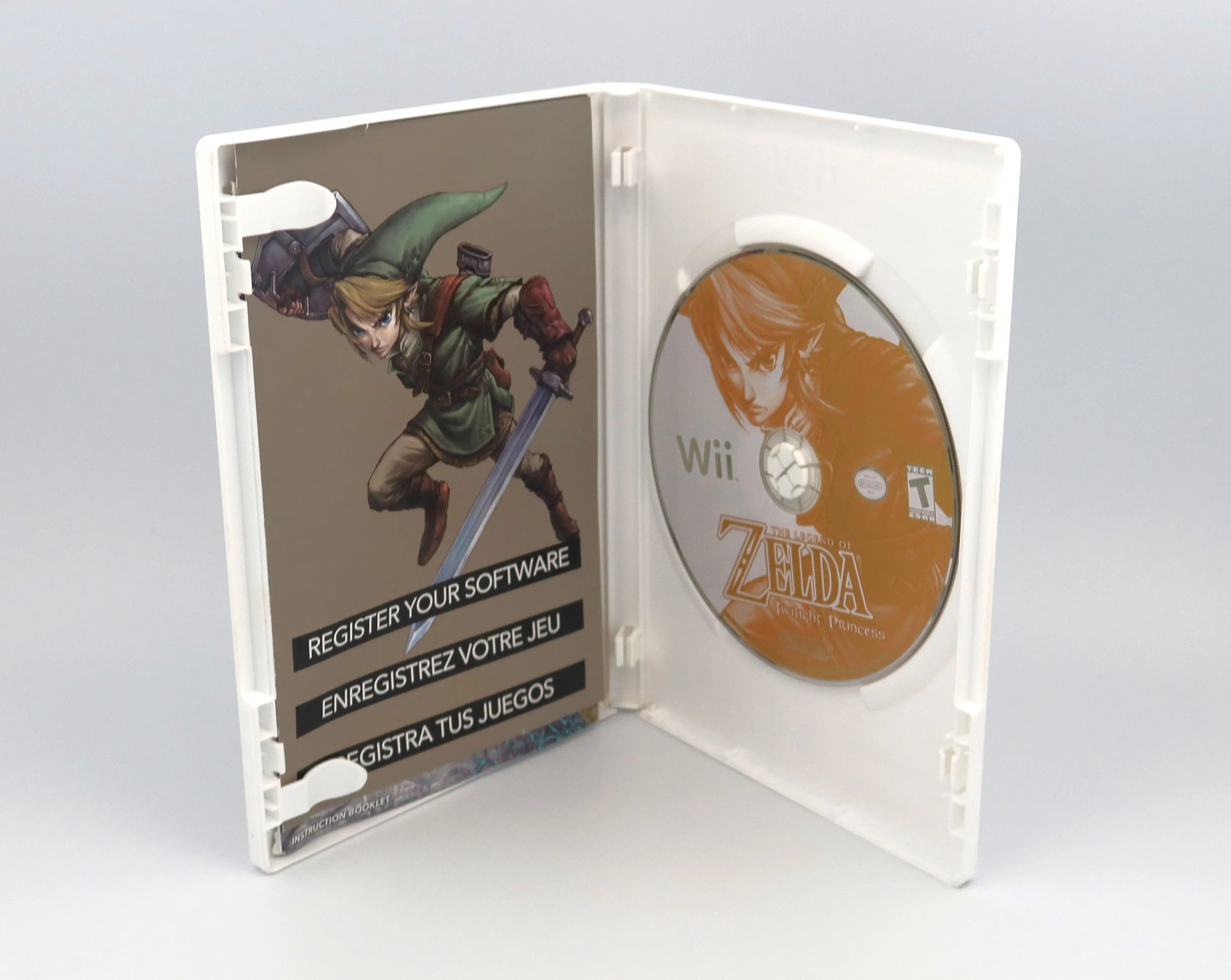 Open case view of a complete in box NTSC-U 2006 copy of The Legend of Zelda Twilight Princess for Nintendo Wii. Showcasing the original Wii case opened displaying authentic Wii game disc and "register your software" insert code on a clean white background.